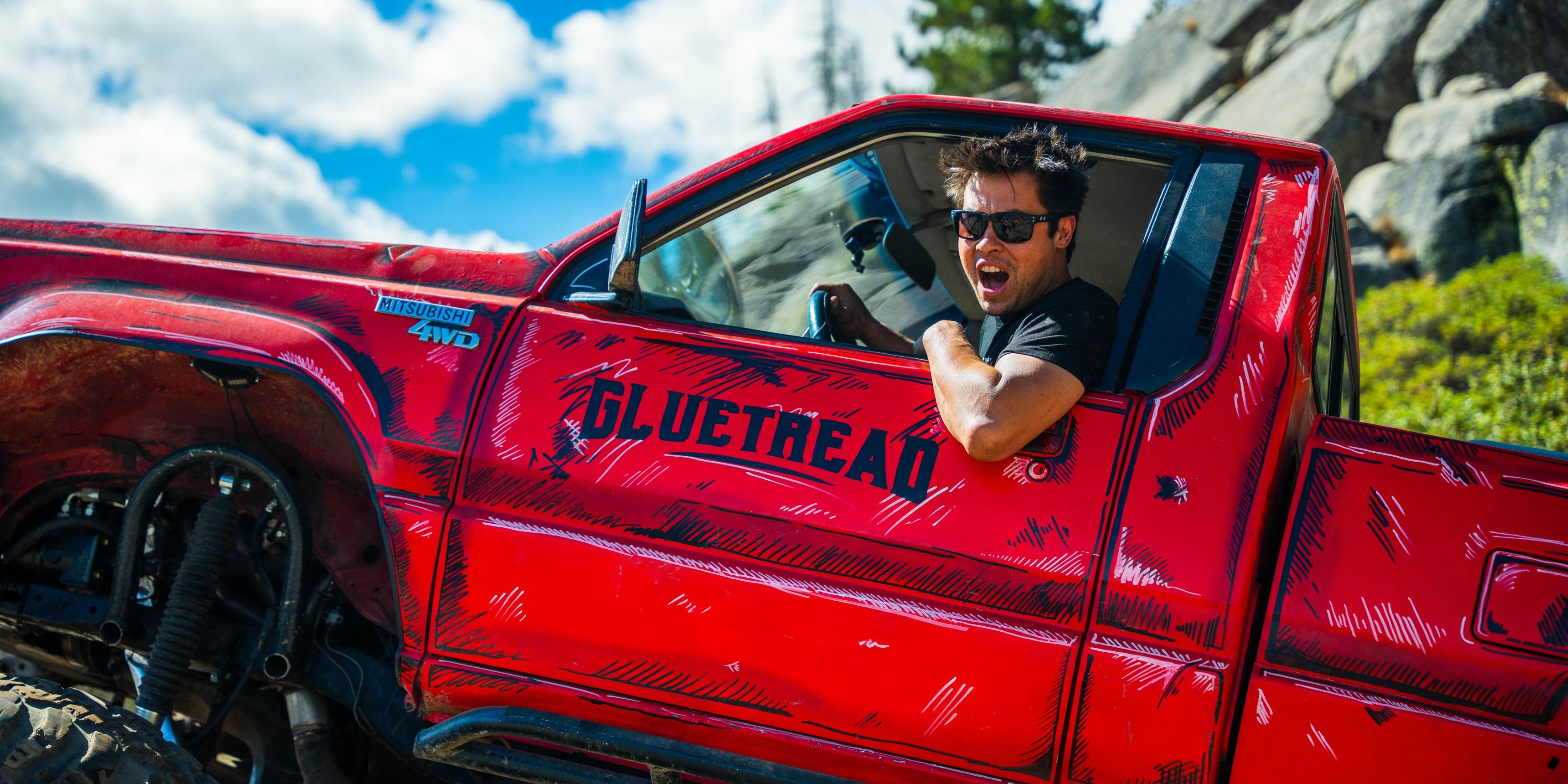 Driver smiling from the window of the GlueTread-branded truck on the Rubicon